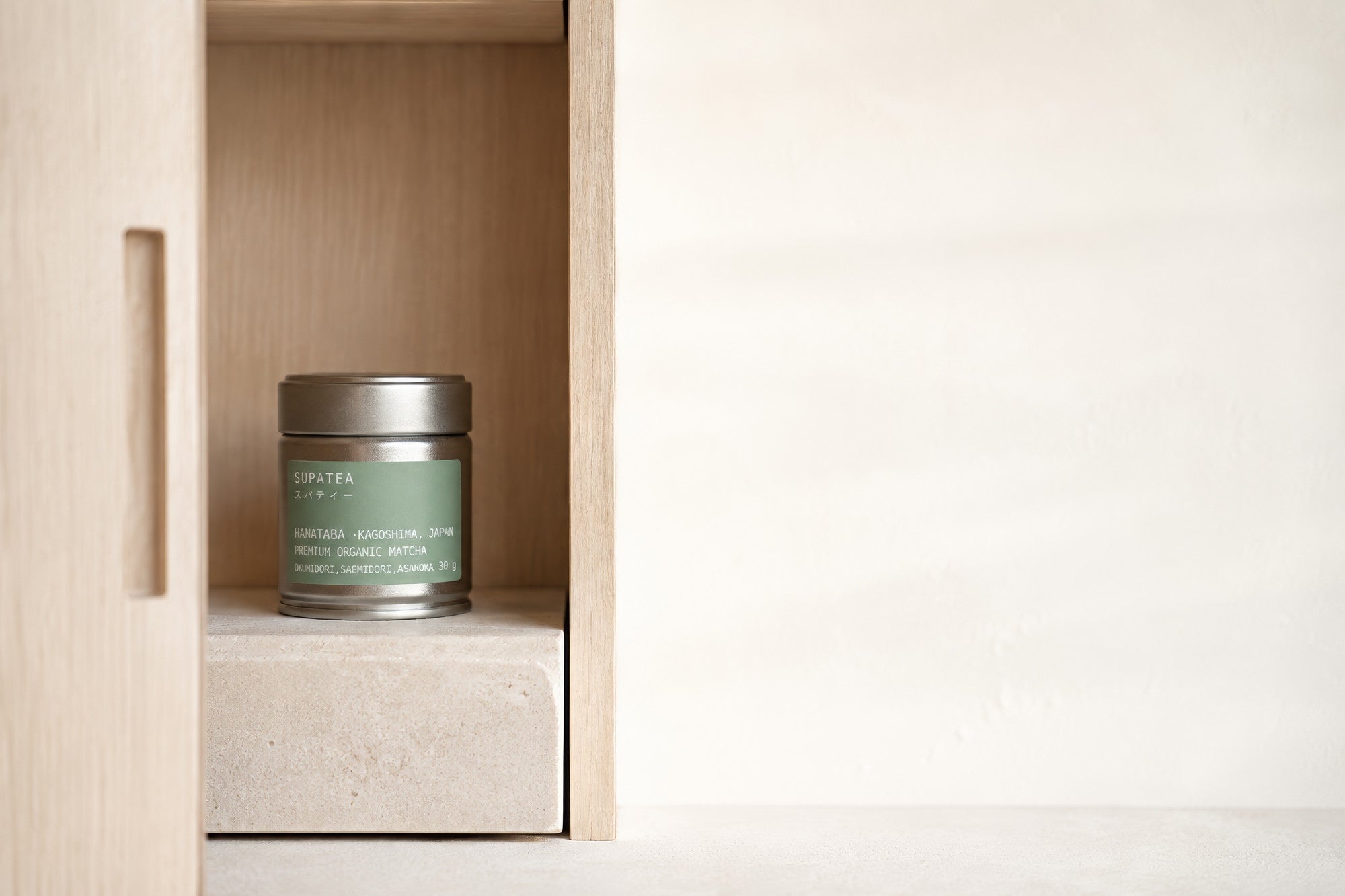 A HANATABA tin standing on a stone block inside a pale wooden cupboard with the door open, away from the light